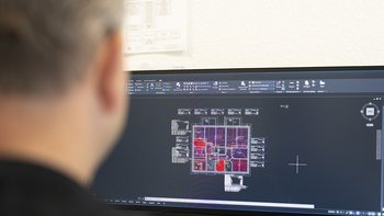 Auf dem Bildschirm sind detaillierte Architekturpläne zu sehen, während ein Mann im Vordergrund daran arbeitet.