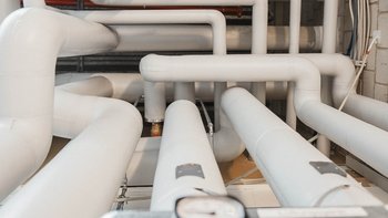 Ein Netzwerk aus weißen Rohren verläuft durch einen Raum, wobei die Rohre in verschiedenen Richtungen angeordnet sind.