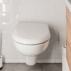 Ein modernes Badezimmer mit einer weißen Toilette, die vor einer hellen Fliesenwand steht, und einem Holzschrank daneben.