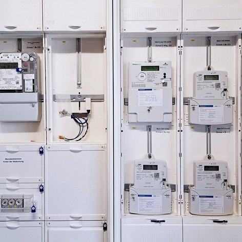 Ein elektrischer Verteiler mit mehreren Zählern und Schaltern, die ordentlich in einem weißen Gehäuse angeordnet sind.