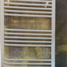 Ein moderner Handtuchwärmer aus weißem Metall steht an einer stilvollen Wand mit goldenen Akzenten.