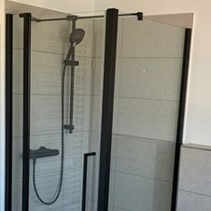 Eine moderne Dusche mit gläserner Trennwand und schwarzem Duschkopf, umgeben von hellen Fliesen und einem Handtuchwärmer.