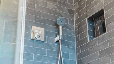 Eine moderne Dusche mit grauen Fliesen, einem eleganten Duschkopf und einem praktischen Ablagefach für Pflegeprodukte.