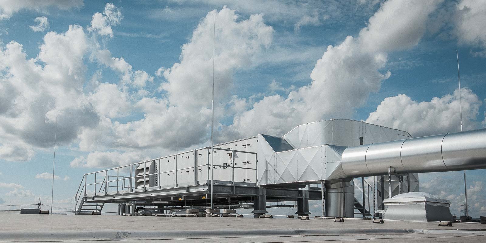 Eine moderne Lüftungsanlage auf einem Dach, umgeben von einem strahlend blauen Himmel mit weißen, fluffigen Wolken.
