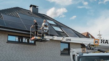 Zwei Männer stehen auf einer Hebebühne und arbeiten an der Installation von Solarpanelen auf einem Dach.
