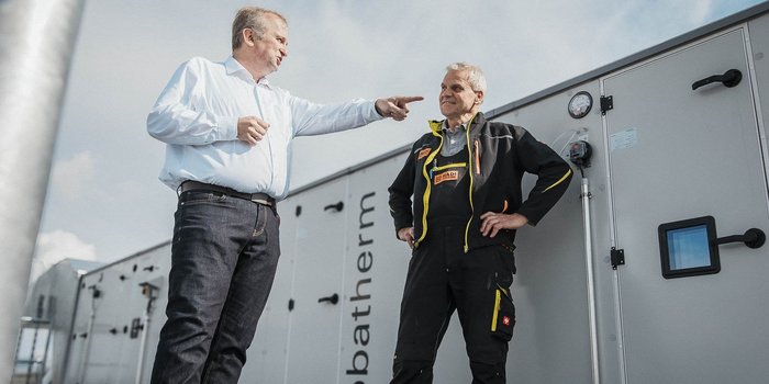 Zwei Männer stehen vor einem großen technischen Gerät, einer zeigt mit dem Finger auf etwas und spricht lebhaft.