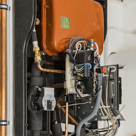 Eine orangefarbene Heizungsanlage mit zahlreichen Rohren und Kabeln, die an einer weißen Wand montiert ist.