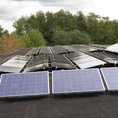 Die Solarpanels auf dem Dach reflektieren das Licht, umgeben von Bäumen, die frisches Grün zeigen.