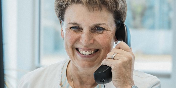 Eine lächelnde Frau mit kurzen Haaren spricht am Telefon und strahlt Freundlichkeit aus.