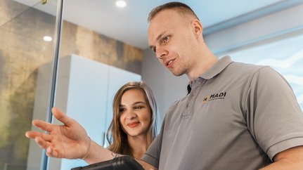 Die beiden Personen scheinen in ein Gespräch vertieft zu sein, während der Mann mit einer Hand auf das Tablet zeigt.