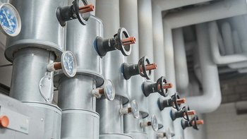 Nahaufnahme von Metallrohren mit blauen Druckanzeigen und schwarzen Ventilen, die in einem modernen Technikraum installiert sind.