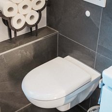 Ein modernes Badezimmer mit einer weißen Toilette und einem blauen Spülkasten, umgeben von grauen Fliesen.
